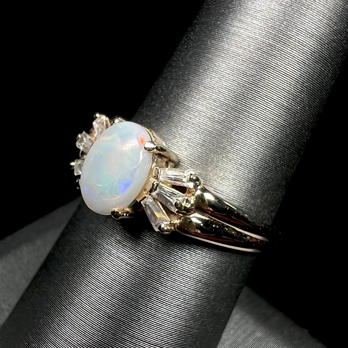 A yellow gold ring set with a natural Australian opal and tapered baguette cut cubic zirconia accents.