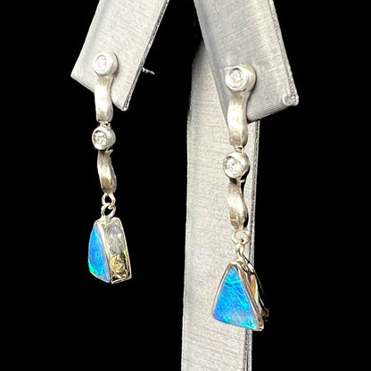 A pair of white gold earrings set with triangle cut natural black opals and round diamond accents.