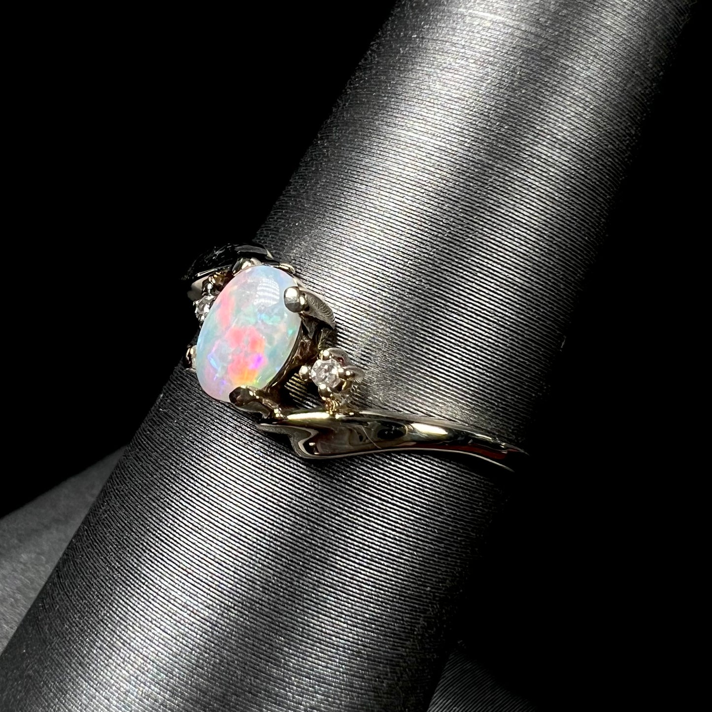 A dainty yellow gold opal and diamond-accented ring.  The opal has red and purple colors.