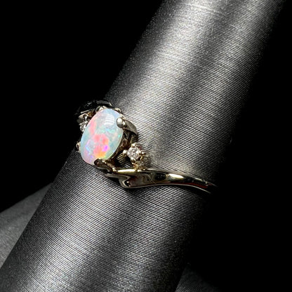 A dainty yellow gold opal and diamond-accented ring.  The opal has red and purple colors.