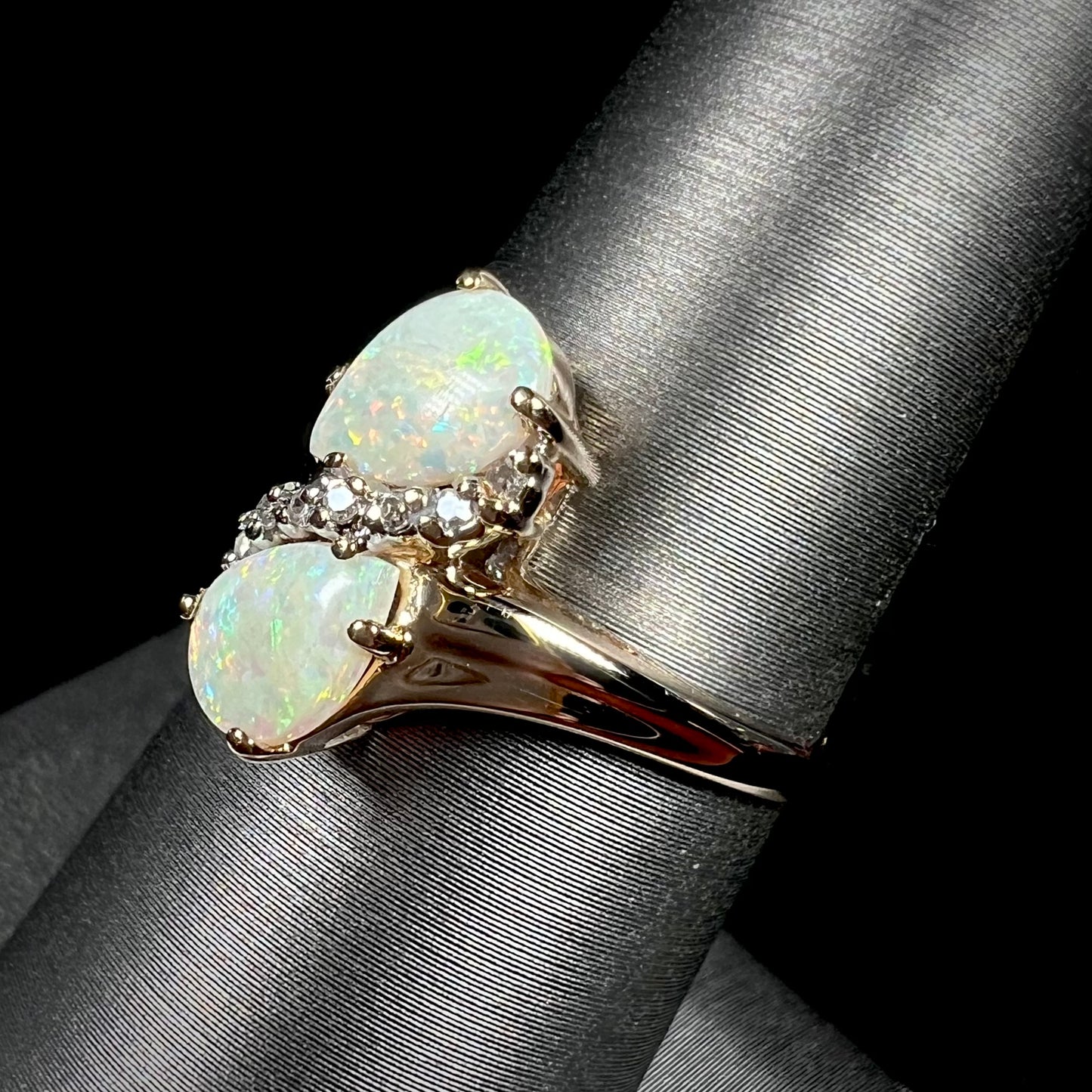 A yellow gold ring mounted with two pear shaped opals and diamond accents  The stones form an infinity shaped design.