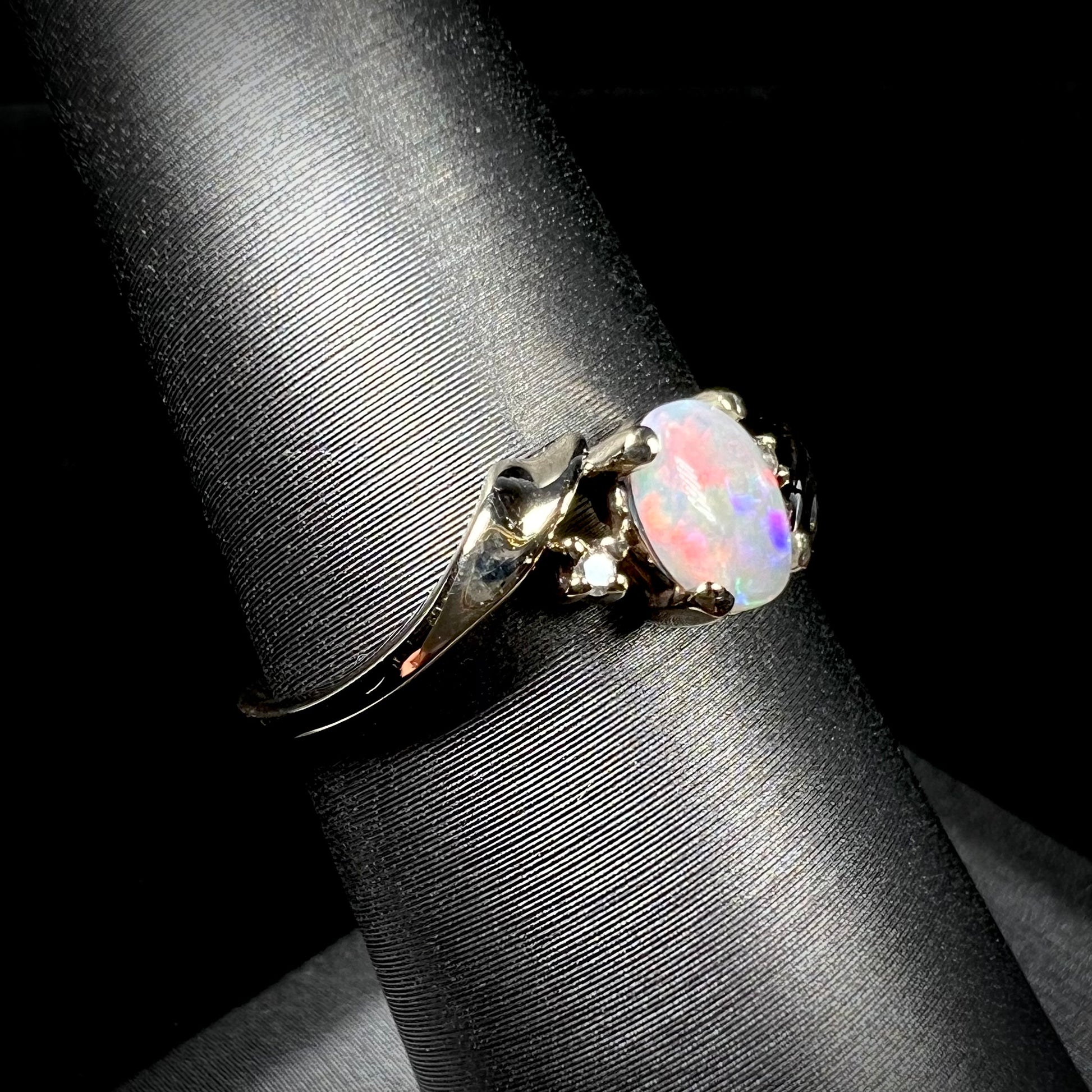 A dainty yellow gold opal and diamond-accented ring.  The opal has red and purple colors.