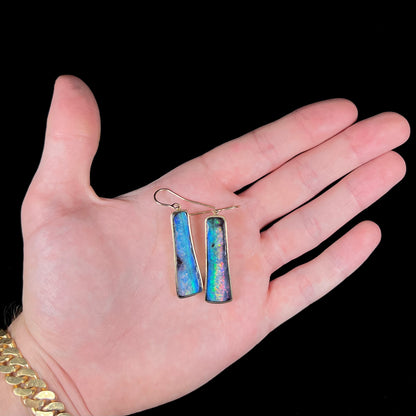 A pair of natural boulder opal dangle earrings set in yellow gold.  The opal displays a rainbow of colors and is from Bull Creek, Australia.