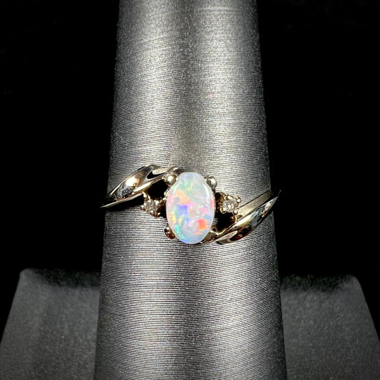 A dainty yellow gold opal and diamond-accented ring.  The opal has red and purple colors.