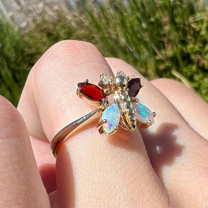 A yellow gold butterfly ring mounted with marquise cut garnets and opals and round diamond accents.