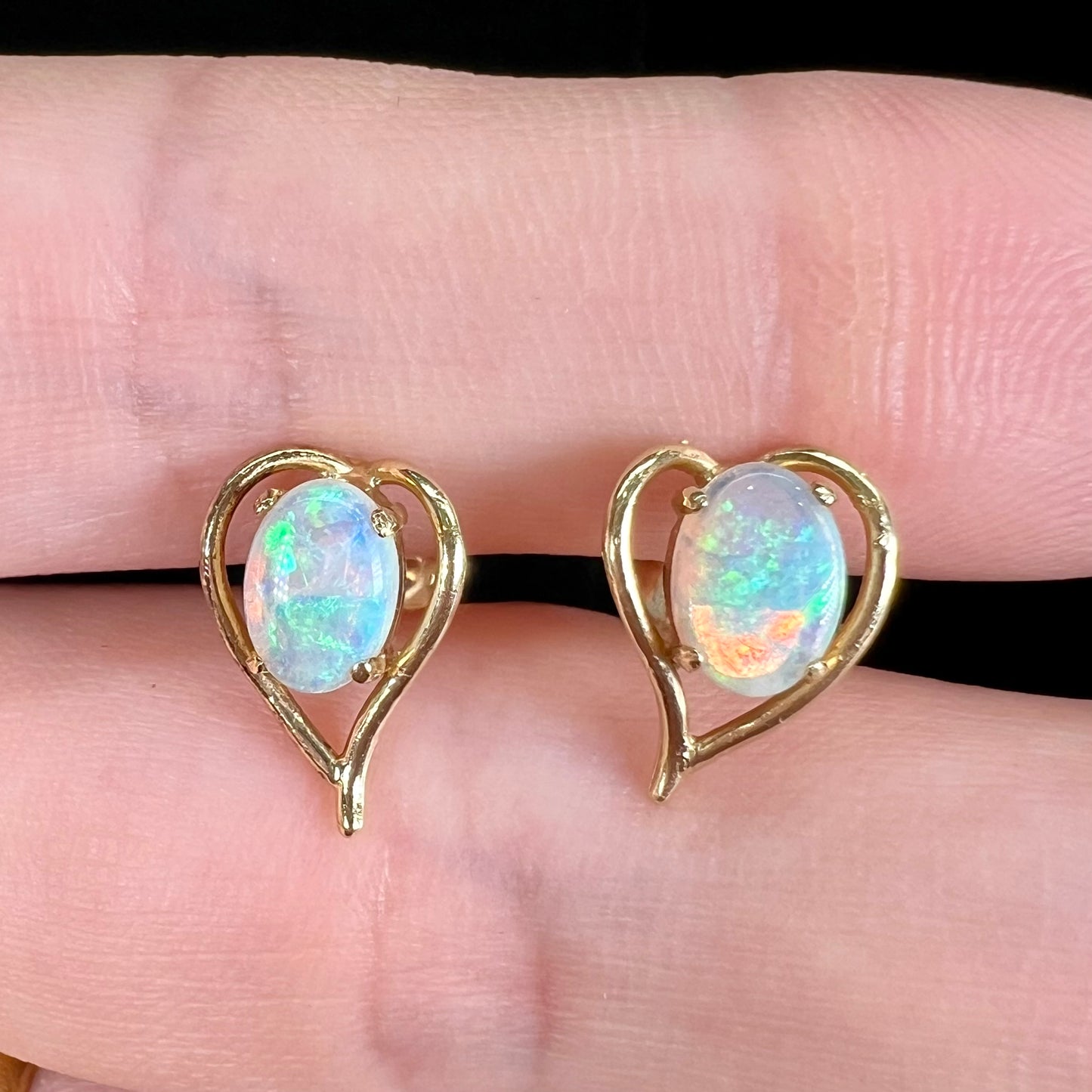 A pair of yellow gold, heart shaped stud earrings set with oval cabochon cut natural opal stones.