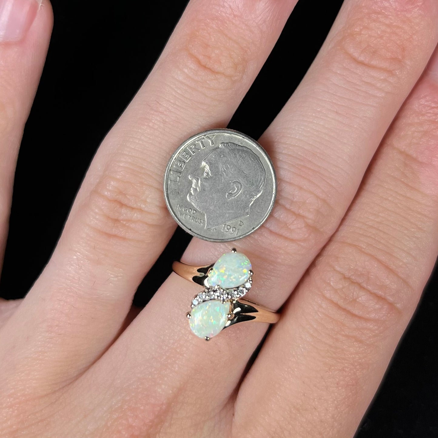 A yellow gold ring mounted with two pear shaped opals and diamond accents  The stones form an infinity shaped design.