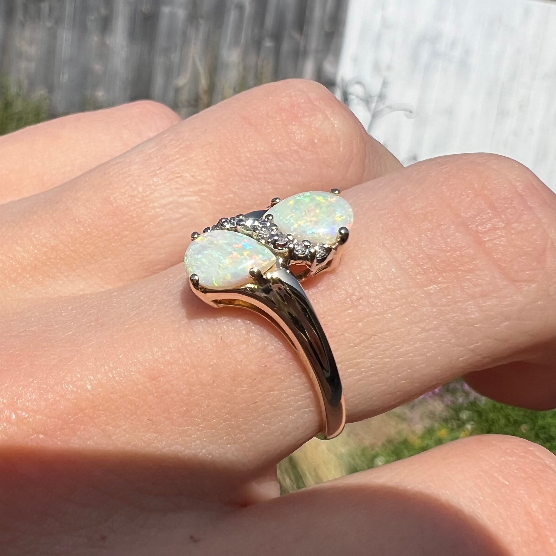 A yellow gold ring mounted with two pear shaped opals and diamond accents  The stones form an infinity shaped design.