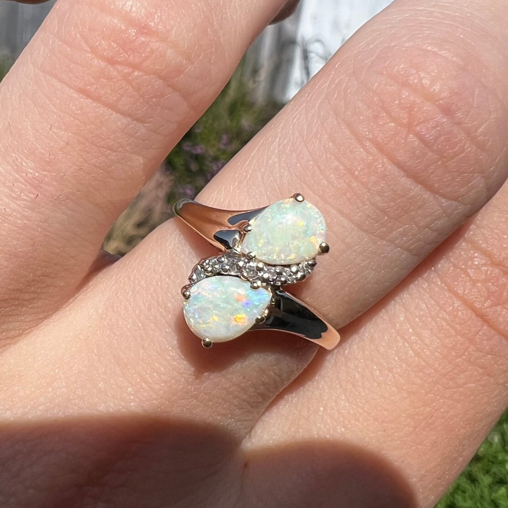 A yellow gold ring mounted with two pear shaped opals and diamond accents  The stones form an infinity shaped design.