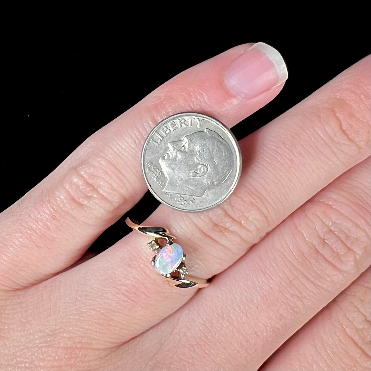 A dainty yellow gold opal and diamond-accented ring.  The opal has red and purple colors.