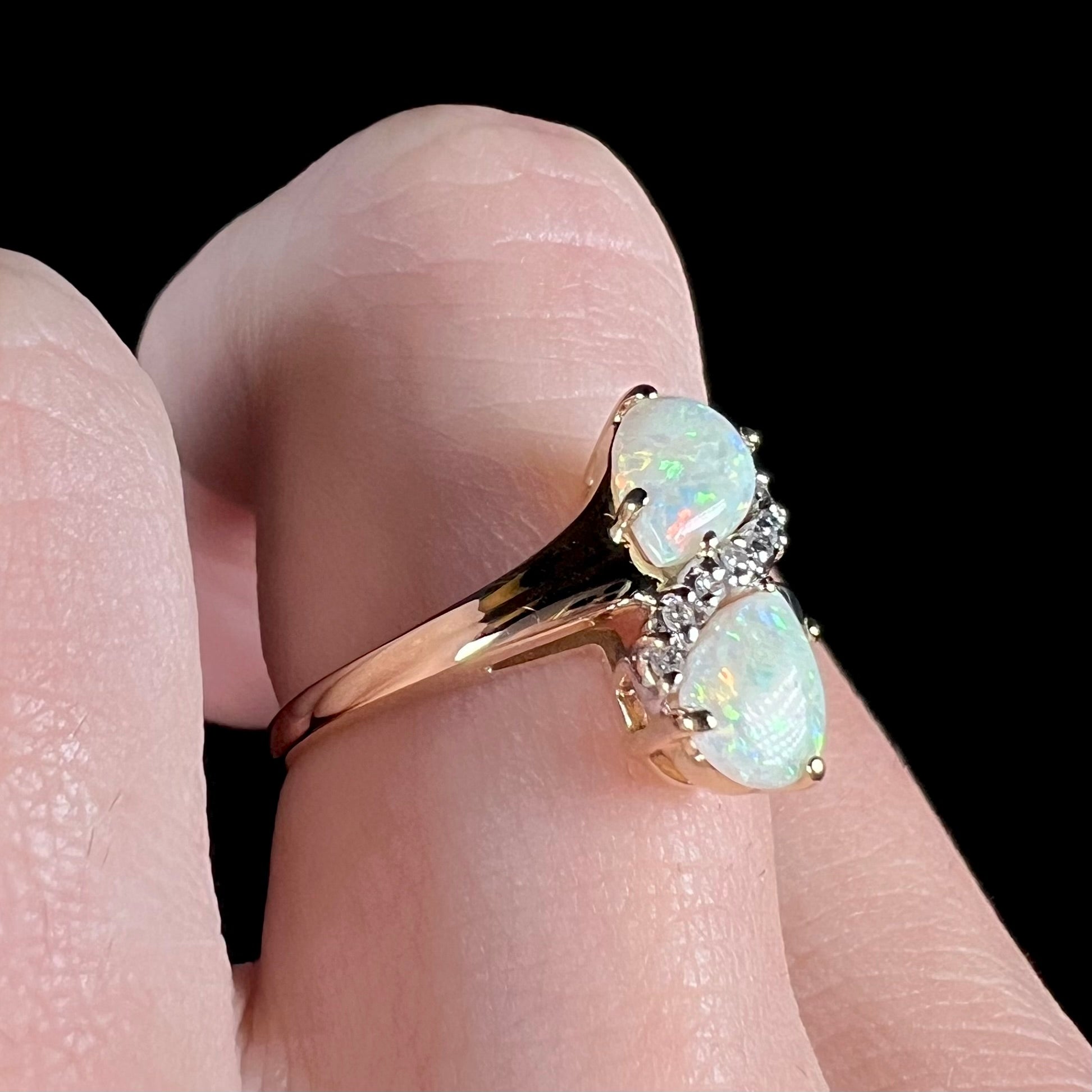 A yellow gold ring mounted with two pear shaped opals and diamond accents  The stones form an infinity shaped design.