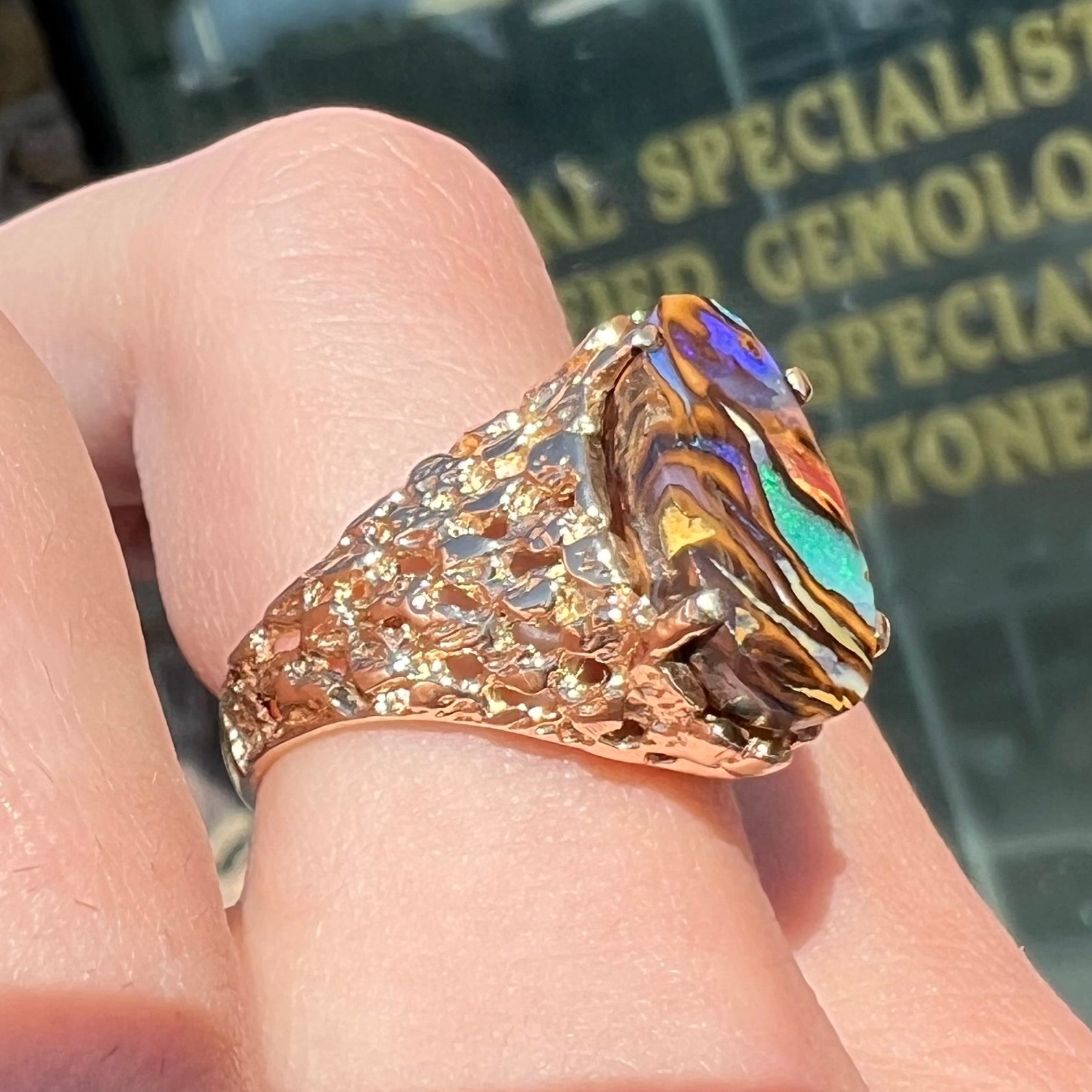 A yellow gold solitaire ring mounted with a Koroit boulder opal stone that shows the picture of a peacock.