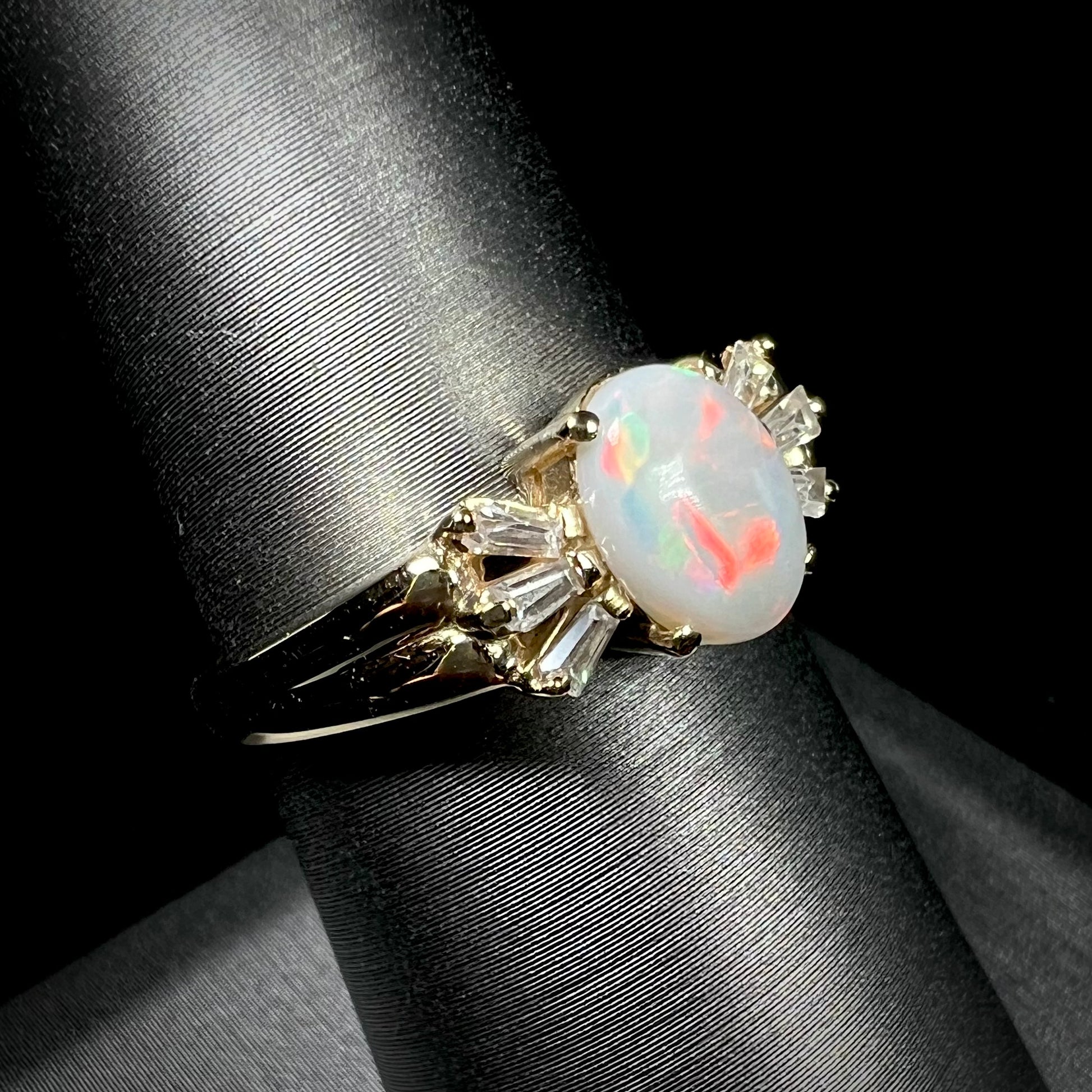 A yellow gold ring set with a natural Australian opal and tapered baguette cut cubic zirconia accents.