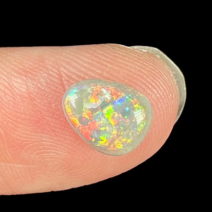 A loose opal cabochon with red, green, orange, and yellow colors.