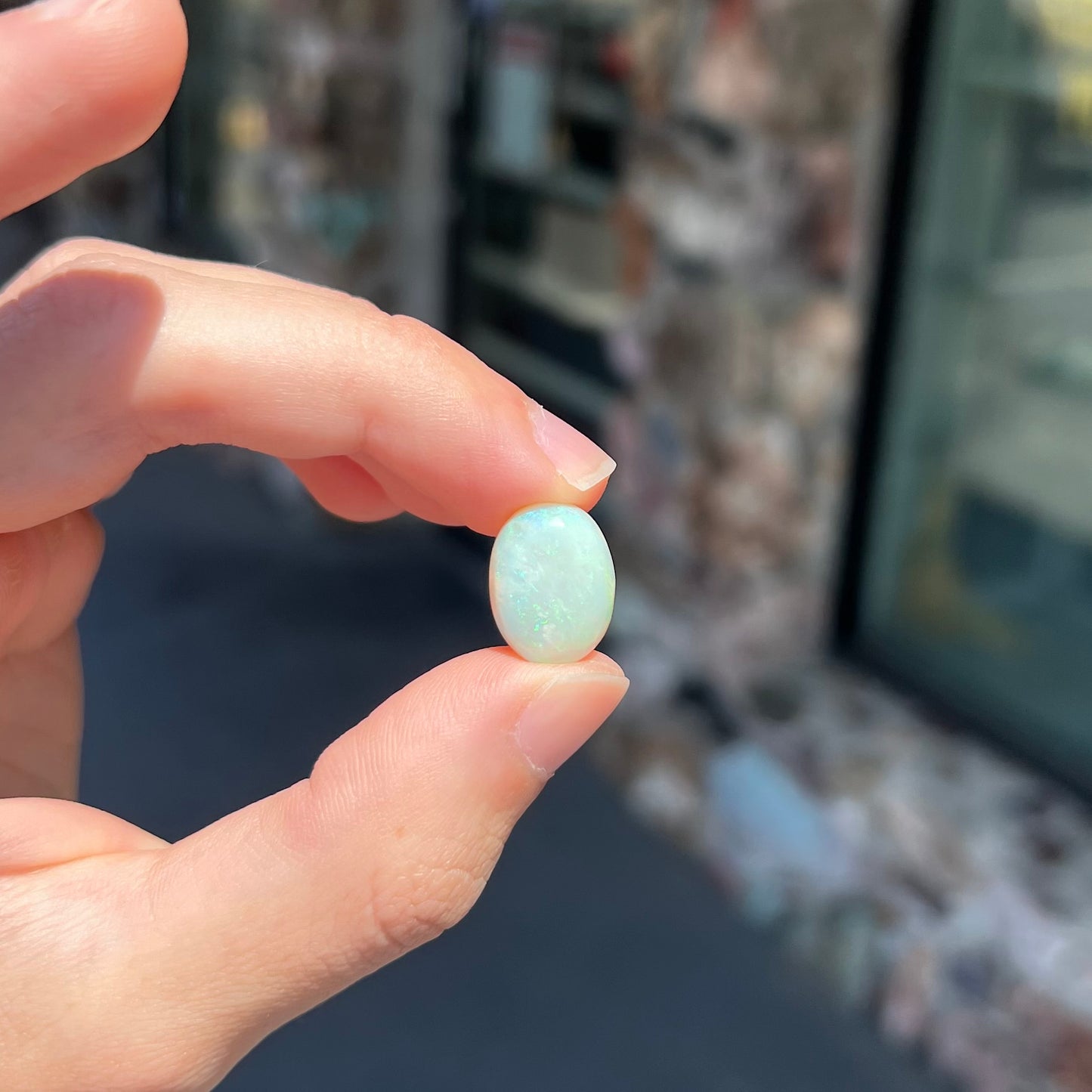 An oval cabochon cut white opal stone from Coober Pedy, Australia.  The opal has subtle colors of green and blue.