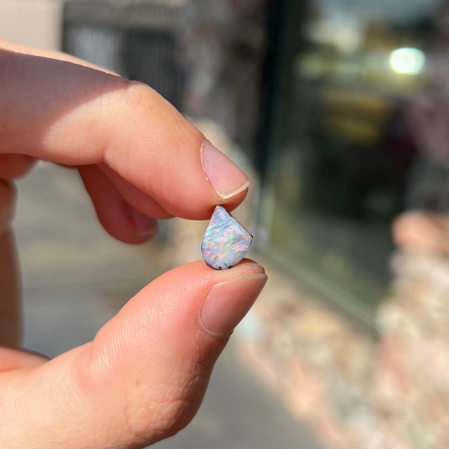 A freeform shaped boulder opal stone with red and blue color play.