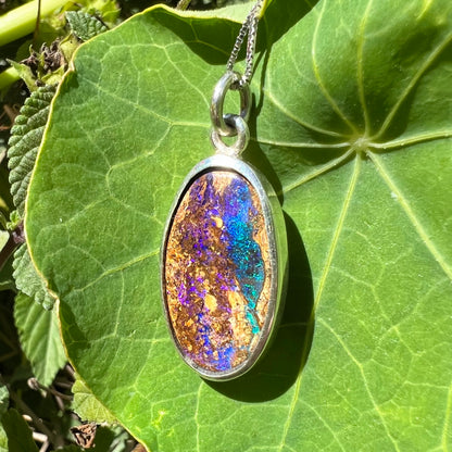 A handmade sterling silver pendant bezel set with an oval cut pipe boulder opal stone.