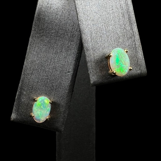 A pair of yellow gold opal stud earrings.  The opals have green and blue fire.