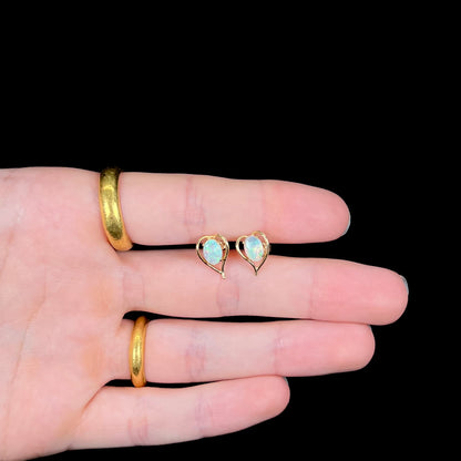 A pair of yellow gold, heart shaped stud earrings set with oval cabochon cut natural opal stones.