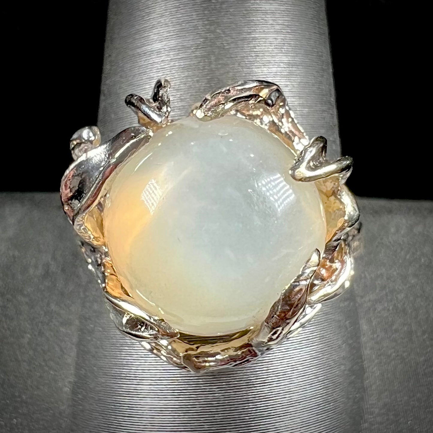 A ladies' organic style white gold moonstone ring.  The moonstone shows white adularescence on a creamy white body color.  Prongs resemble leaves holding the stone.