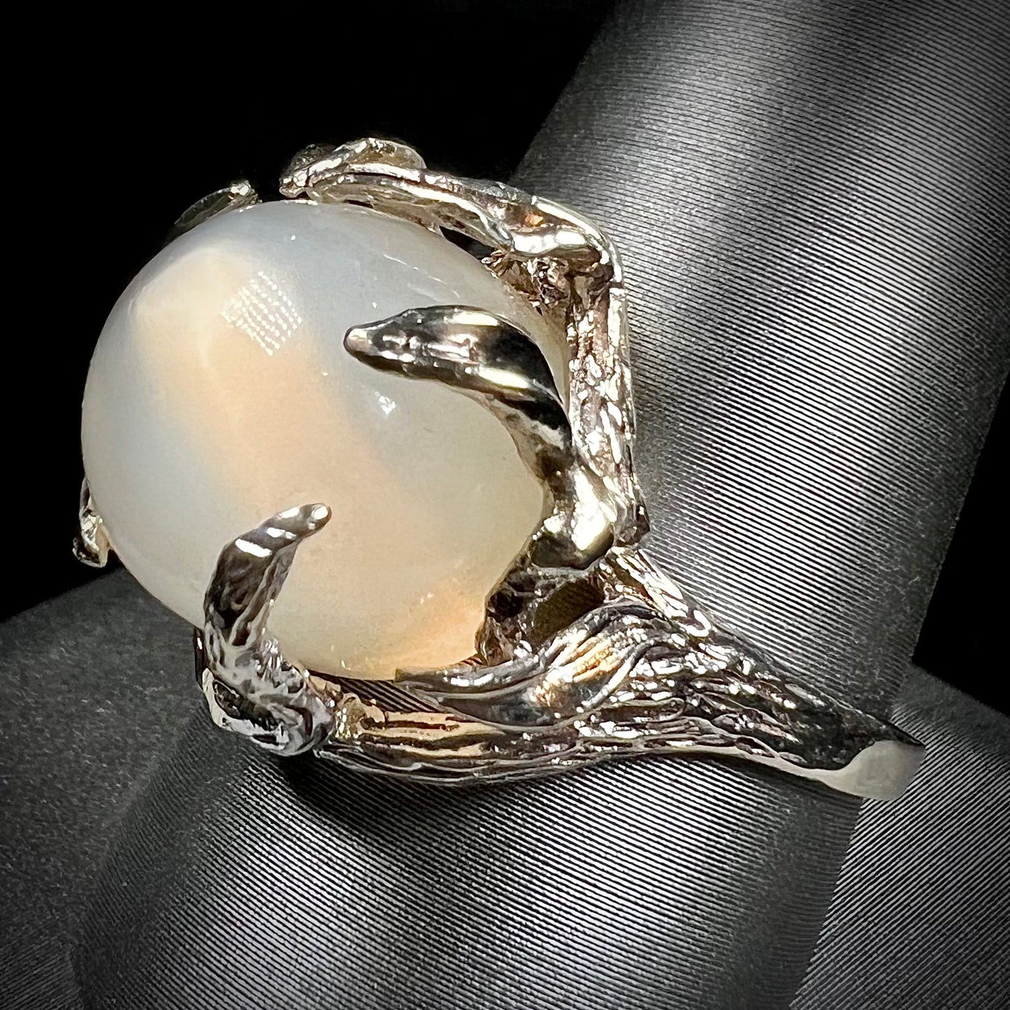 A ladies' organic style white gold moonstone ring.  The moonstone shows white adularescence on a creamy white body color.  Prongs resemble leaves holding the stone.