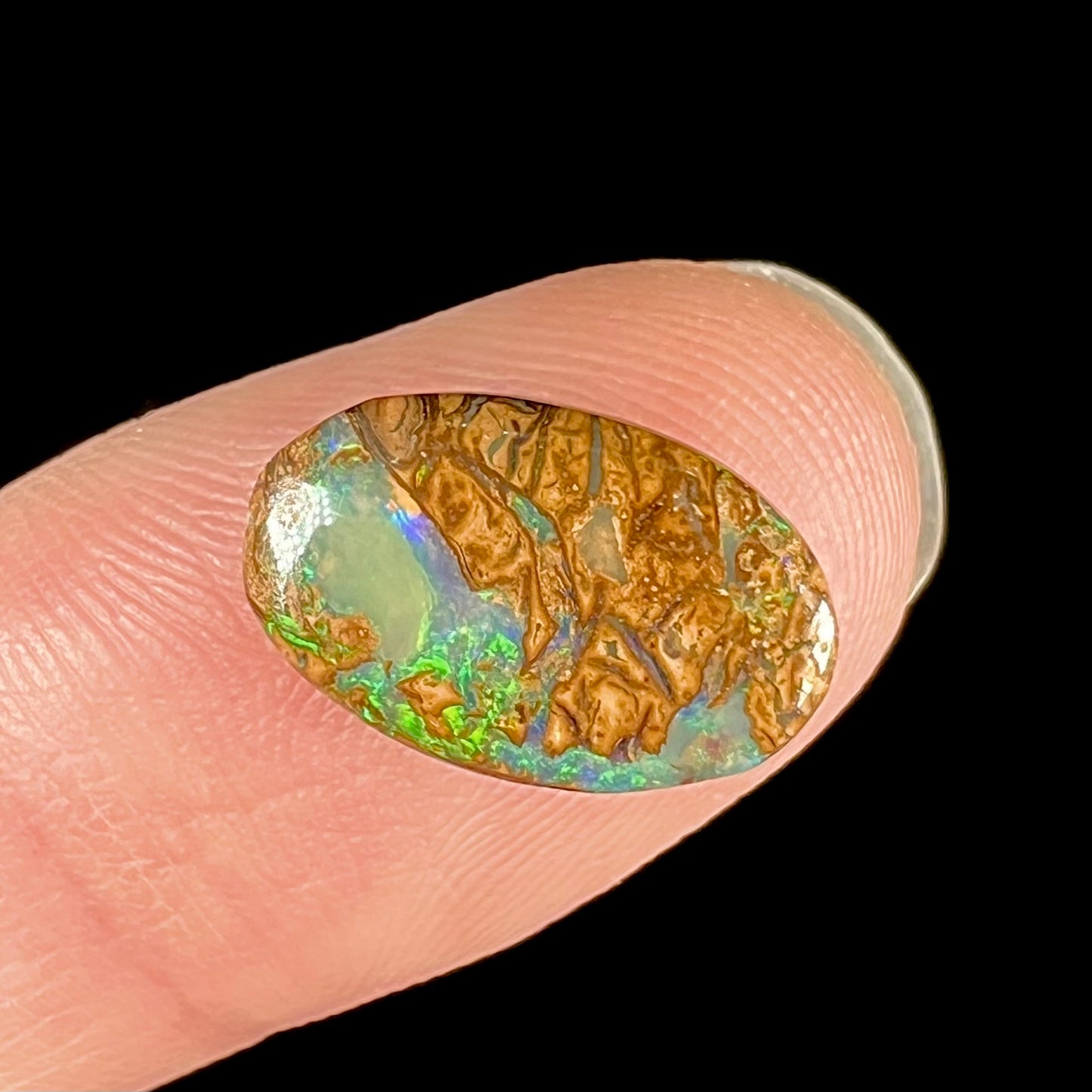 A loose, oval cabochon cut Koroit boulder opal with green fire.