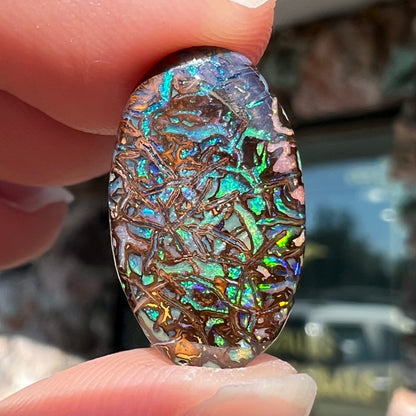 A loose, oval cabochon cut Koroit boulder opal stone.  The opal has green and blue veins.