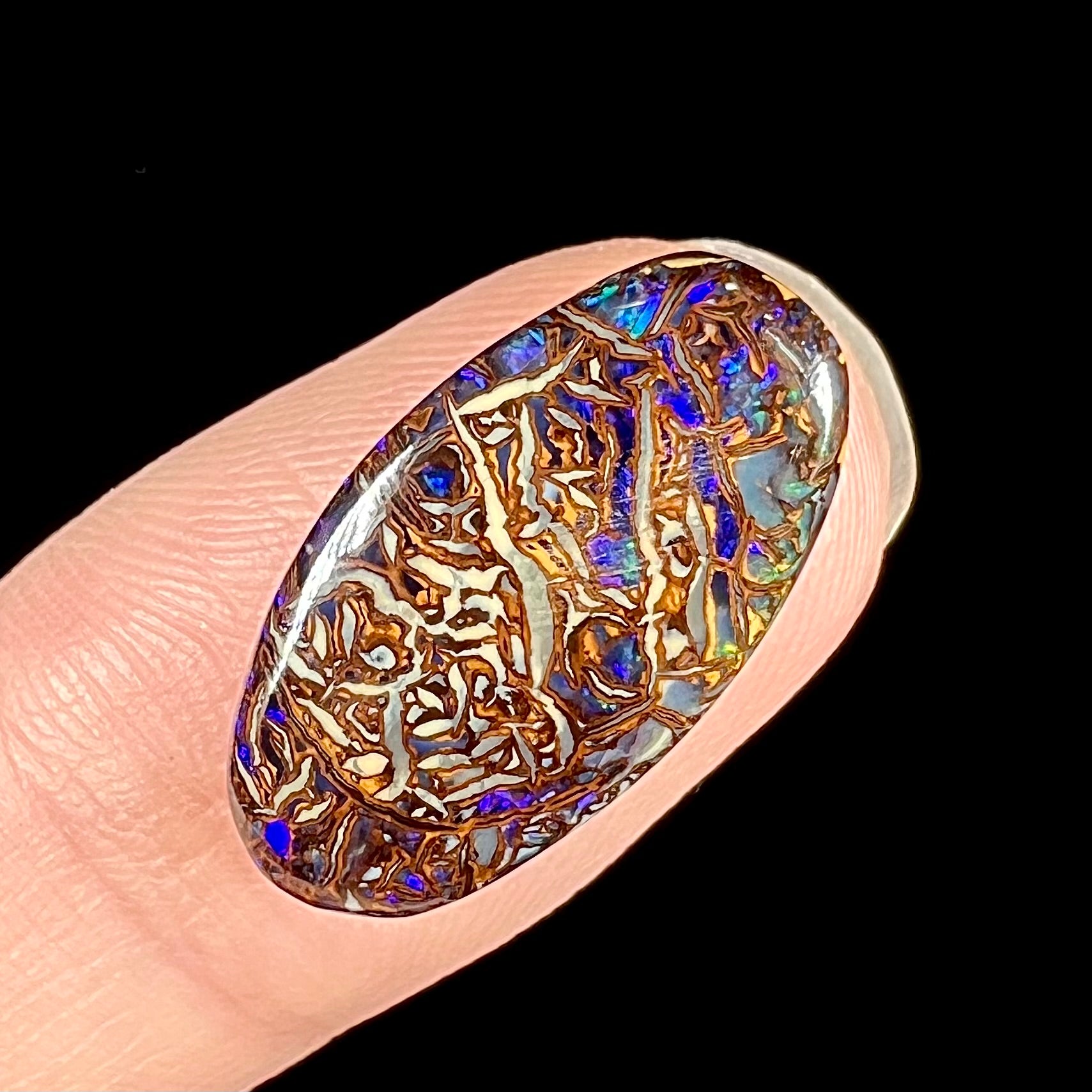 An oval cabochon cut Koroit boulder matrix opal stone.  The opal has blue colors.