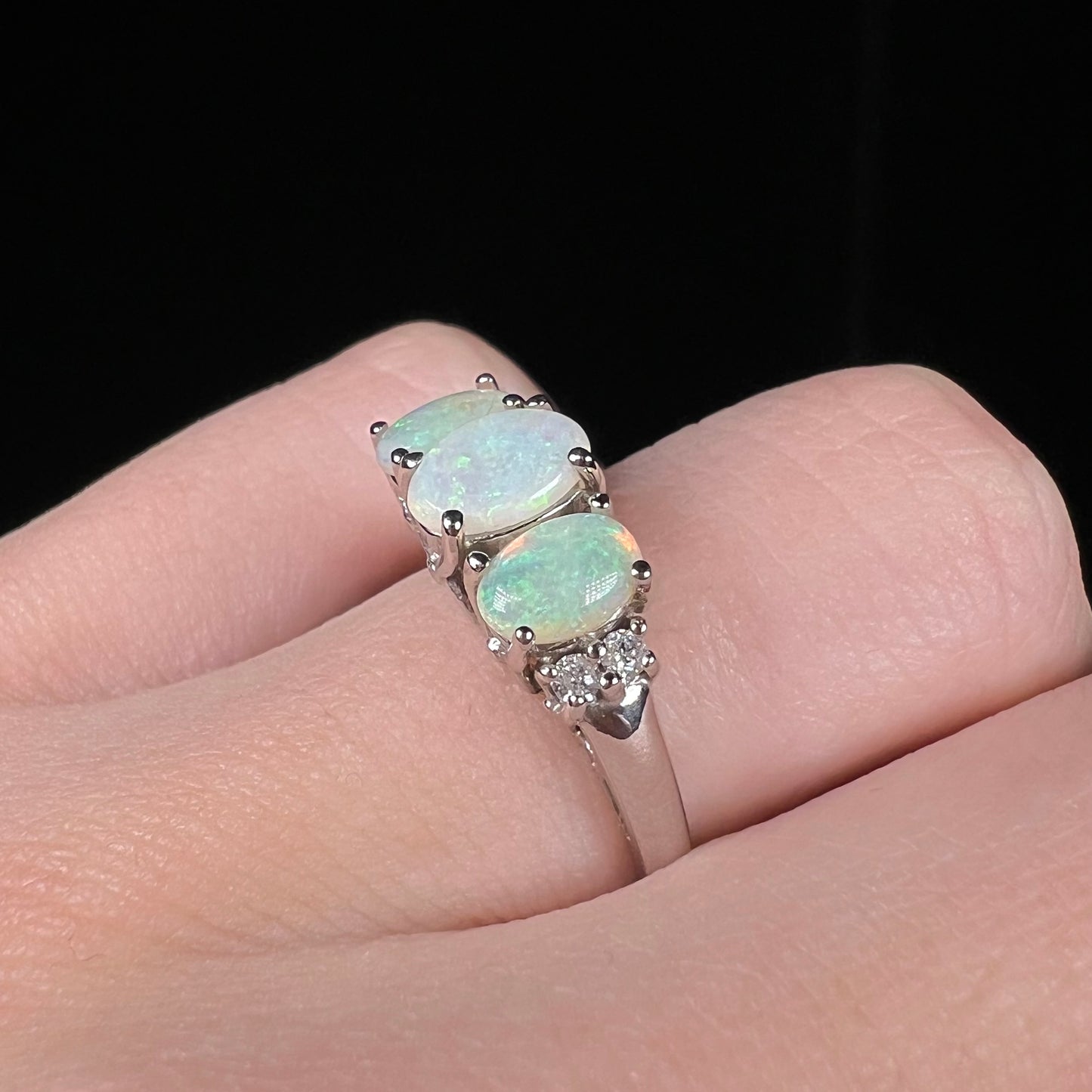 A ladies' white gold ring prong-set with three natural white opals and diamond accents.  The opals play a green color.