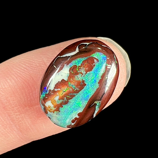 A loose, oval cabochon cut boulder opal stone from Australia.  The opal has blue and green veins in an ironstone matrix.