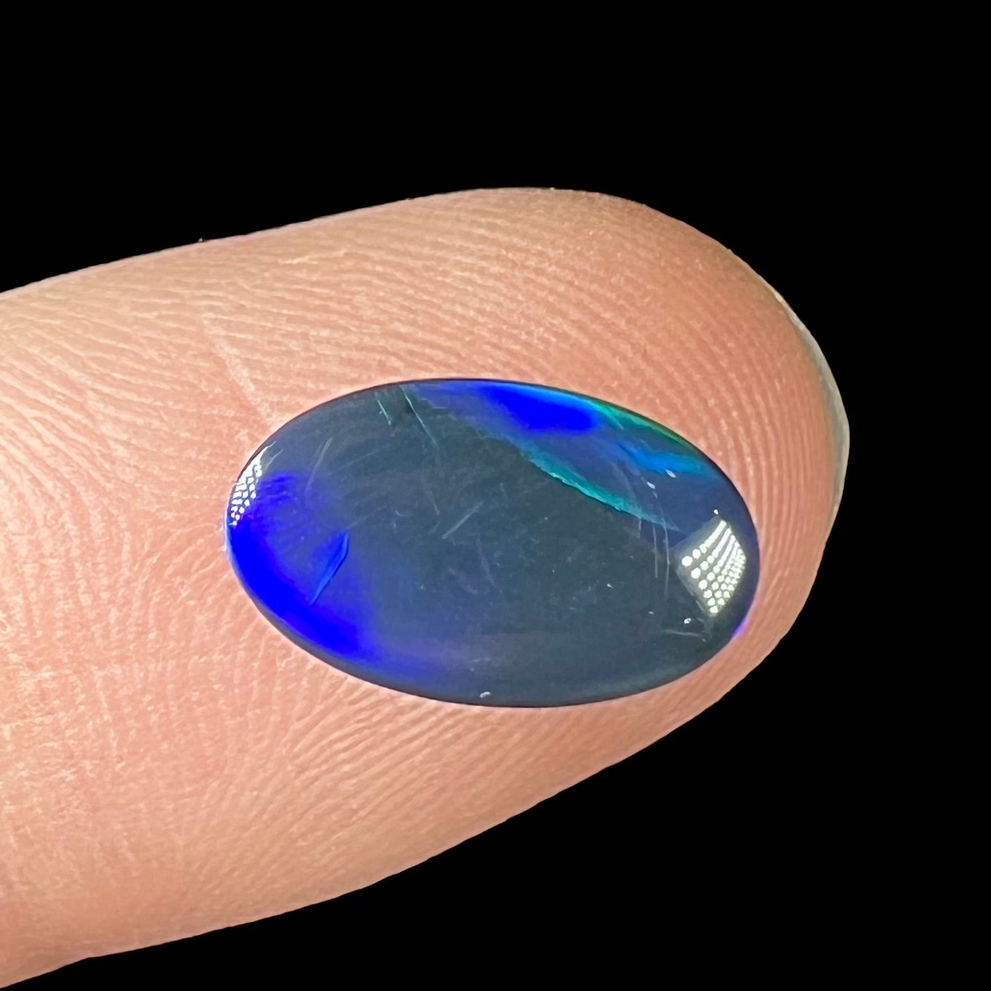 A loose, oval cabochon cut black opal from Lightning Ridge, Australia.  The opal has an N2 body tone.