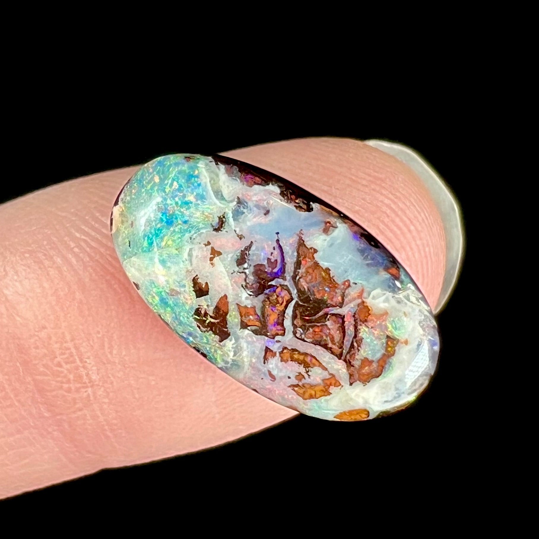 An oval cabochon cut boulder opal stone from Koroit, Australia.  The opal has a white body tone.