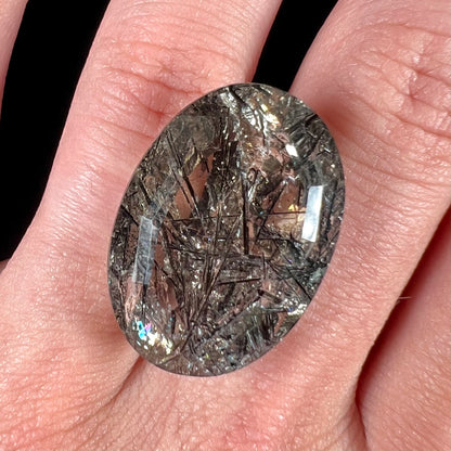 A loose, faceted oval cut smoky quartz stone with black tourmaline crystal inclusions.