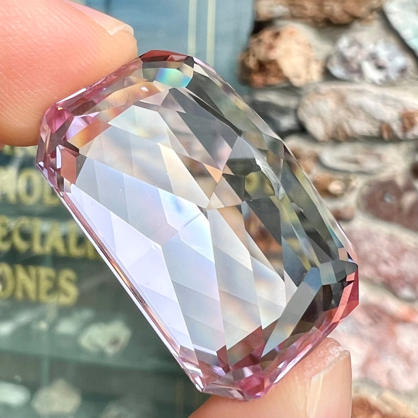 A loose, radiant cut kunzite gemstone.  The stone is a light purplish pink color.