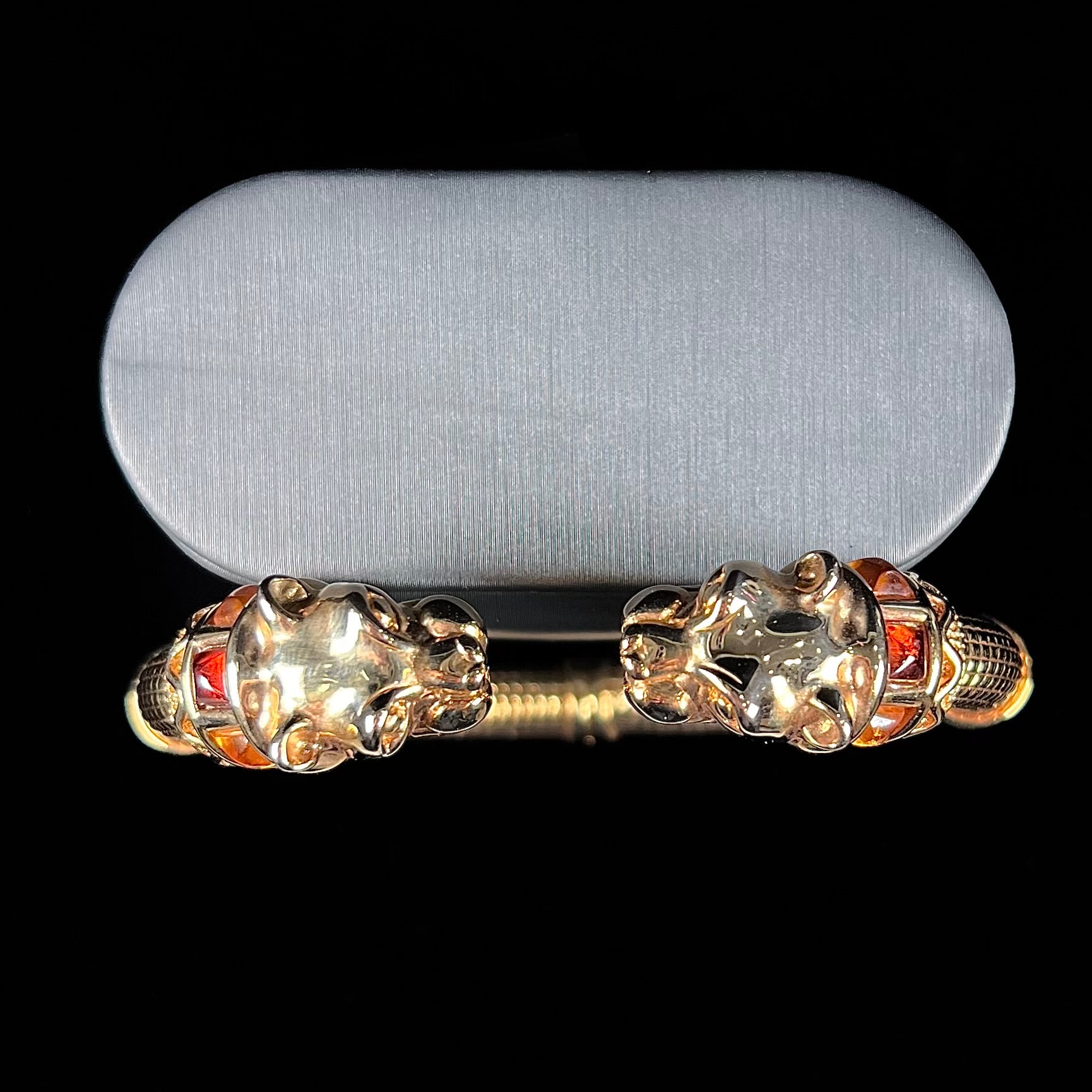 A 14 karat yellow gold hinged bangle bracelet featuring the motif of two panther heads.  There are yellow and red accent stones.