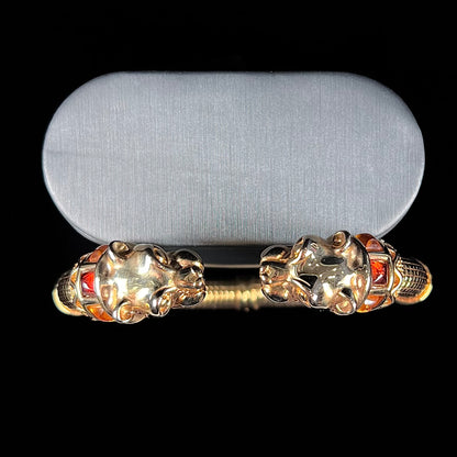 A 14 karat yellow gold hinged bangle bracelet featuring the motif of two panther heads.  There are yellow and red accent stones.