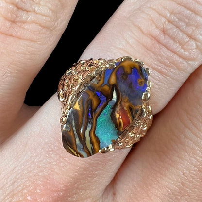 A yellow gold solitaire ring mounted with a Koroit boulder opal stone that shows the picture of a peacock.