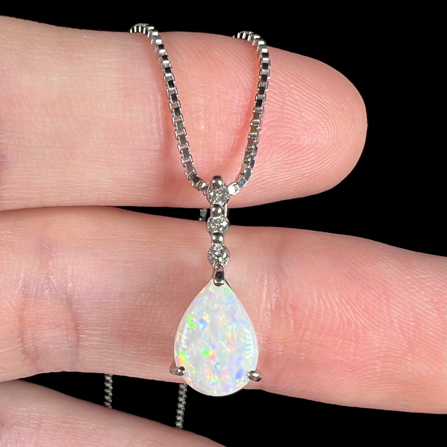 A platinum drop pendant mounted with three diamond accents and a pear shaped opal.