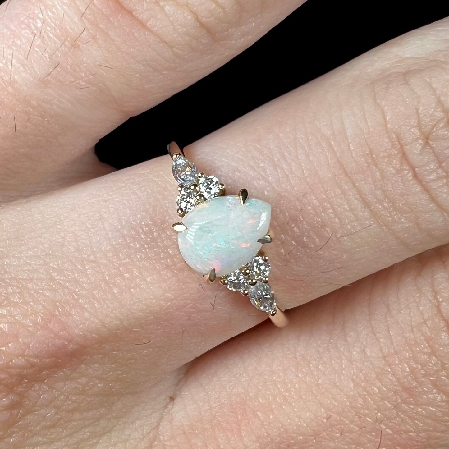 A dainty, pear shaped opal ring mounted in yellow gold with moissanite accents.