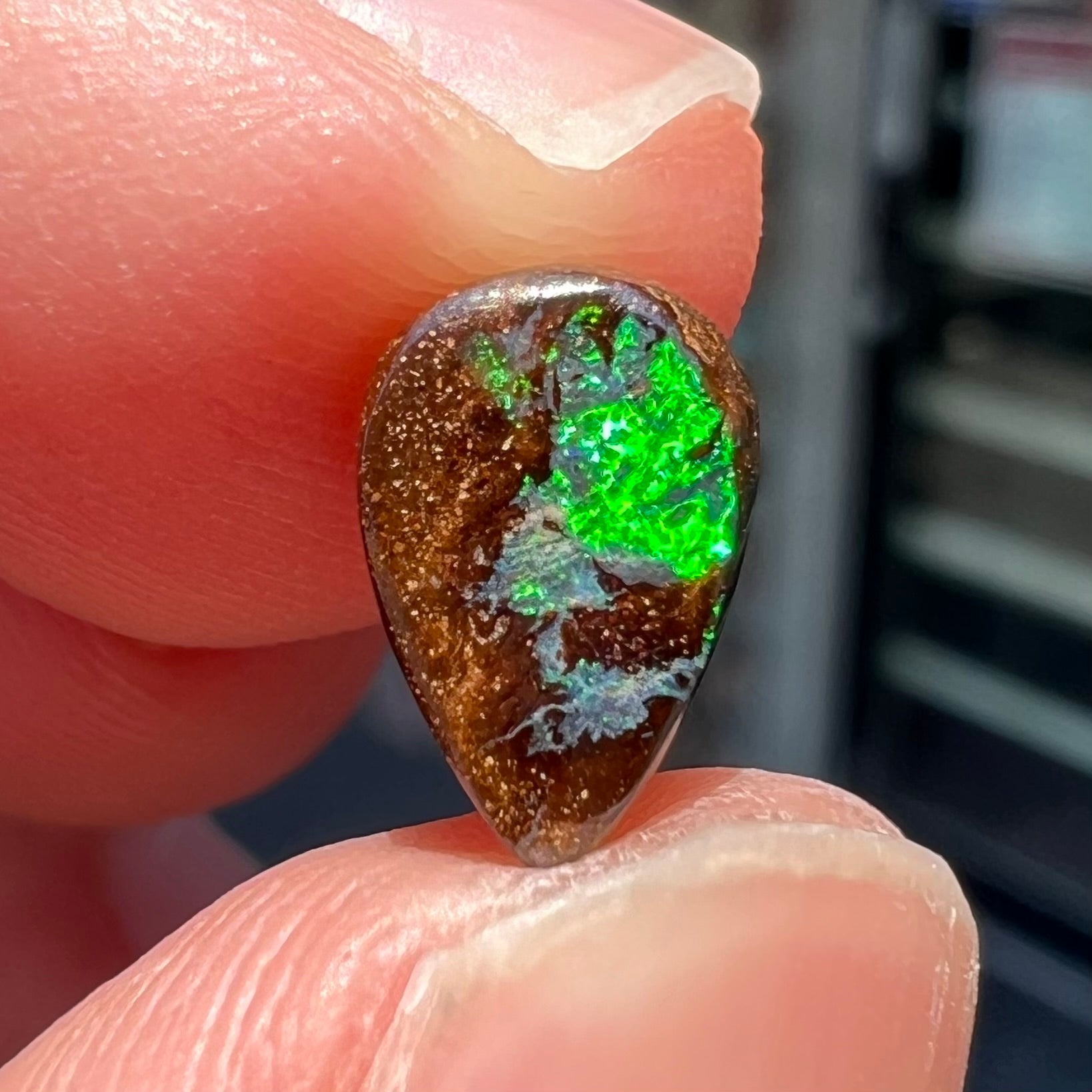 A loose, pear shaped boulder opal stone that flashes colors of green and blue.