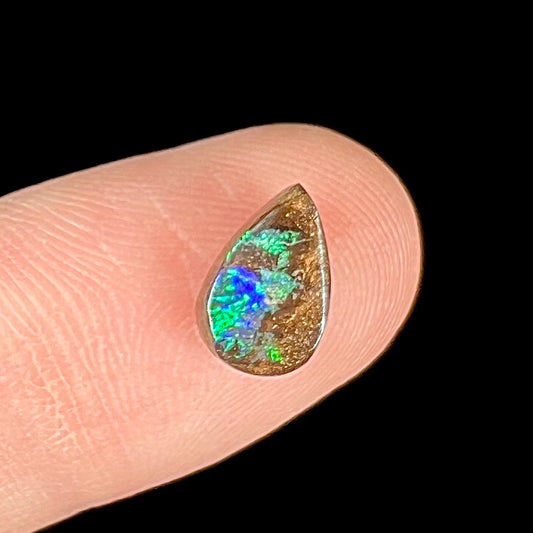 A loose, pear shaped boulder opal stone that flashes colors of green and blue.
