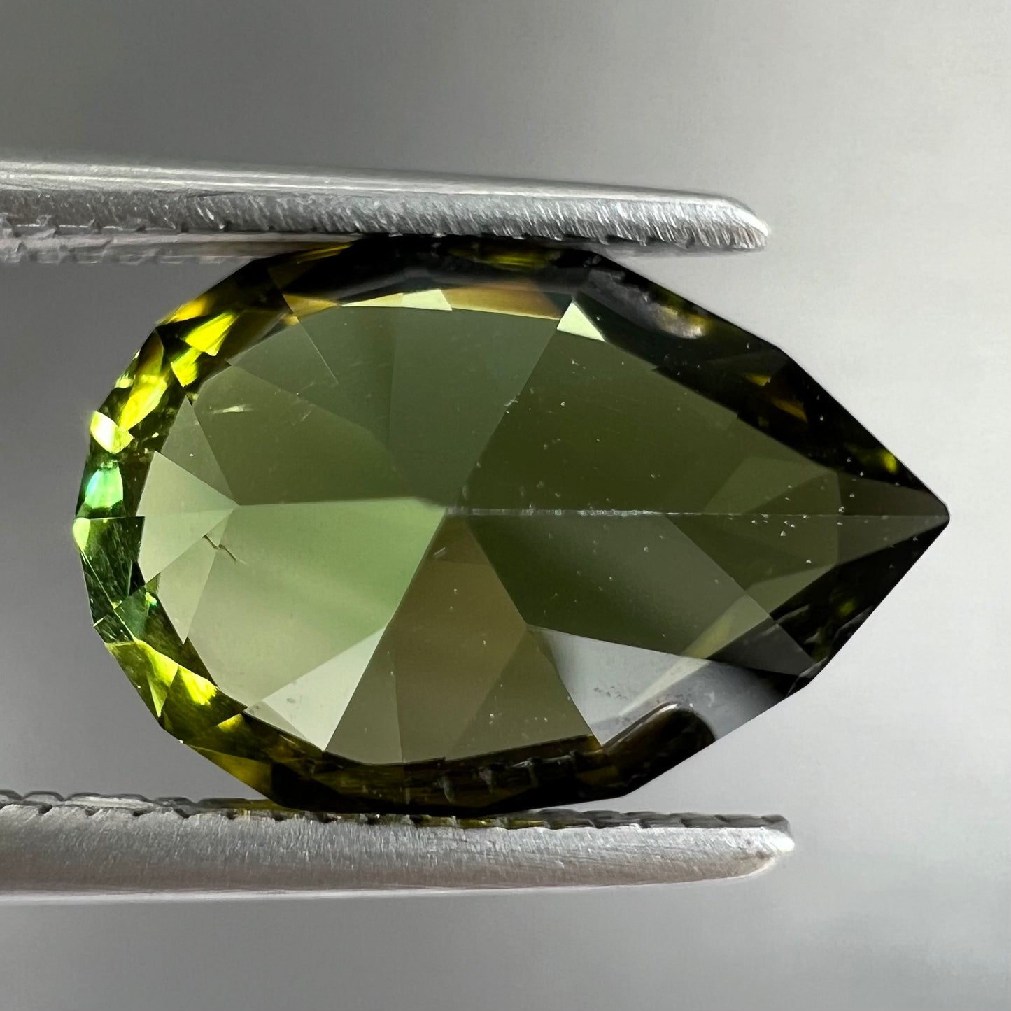 A loose, pear shaped green tourmaline gemstone.  The color is dark green with a yellow secondary hue.