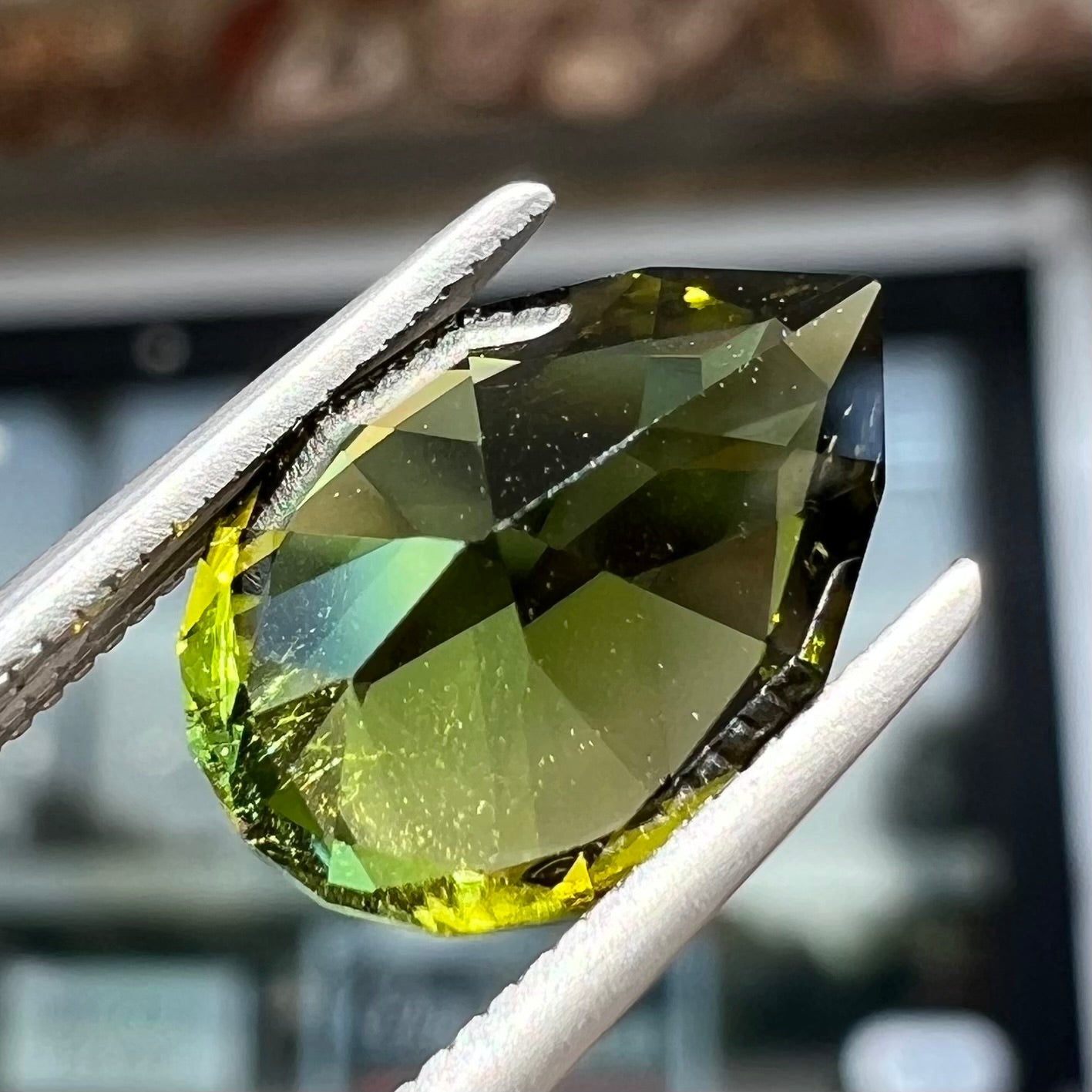 A loose, pear shaped green tourmaline gemstone.  The color is dark green with a yellow secondary hue.