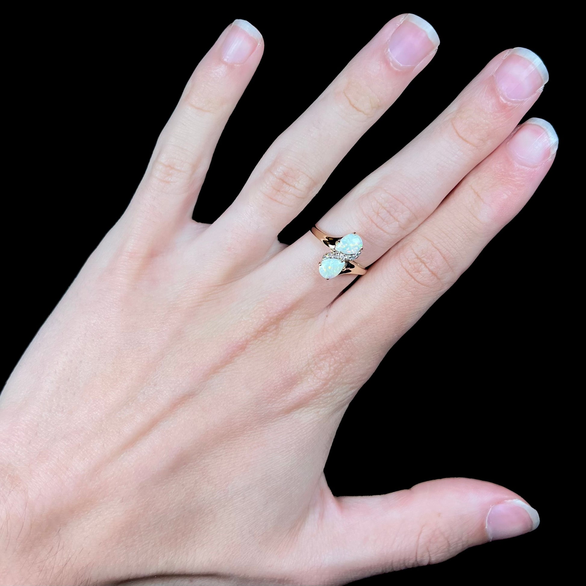 A yellow gold ring mounted with two pear shaped opals and diamond accents  The stones form an infinity shaped design.