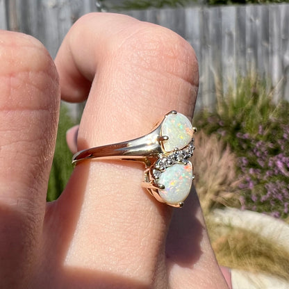 A yellow gold ring mounted with two pear shaped opals and diamond accents  The stones form an infinity shaped design.