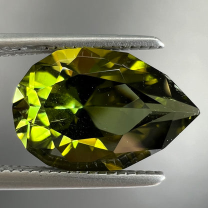 A loose, pear shaped green tourmaline gemstone.  The color is dark green with a yellow secondary hue.