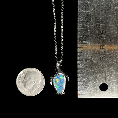 A sterling silver penguin necklace inlaid with a black opal doublet and a CZ accent in the penguin's eye.