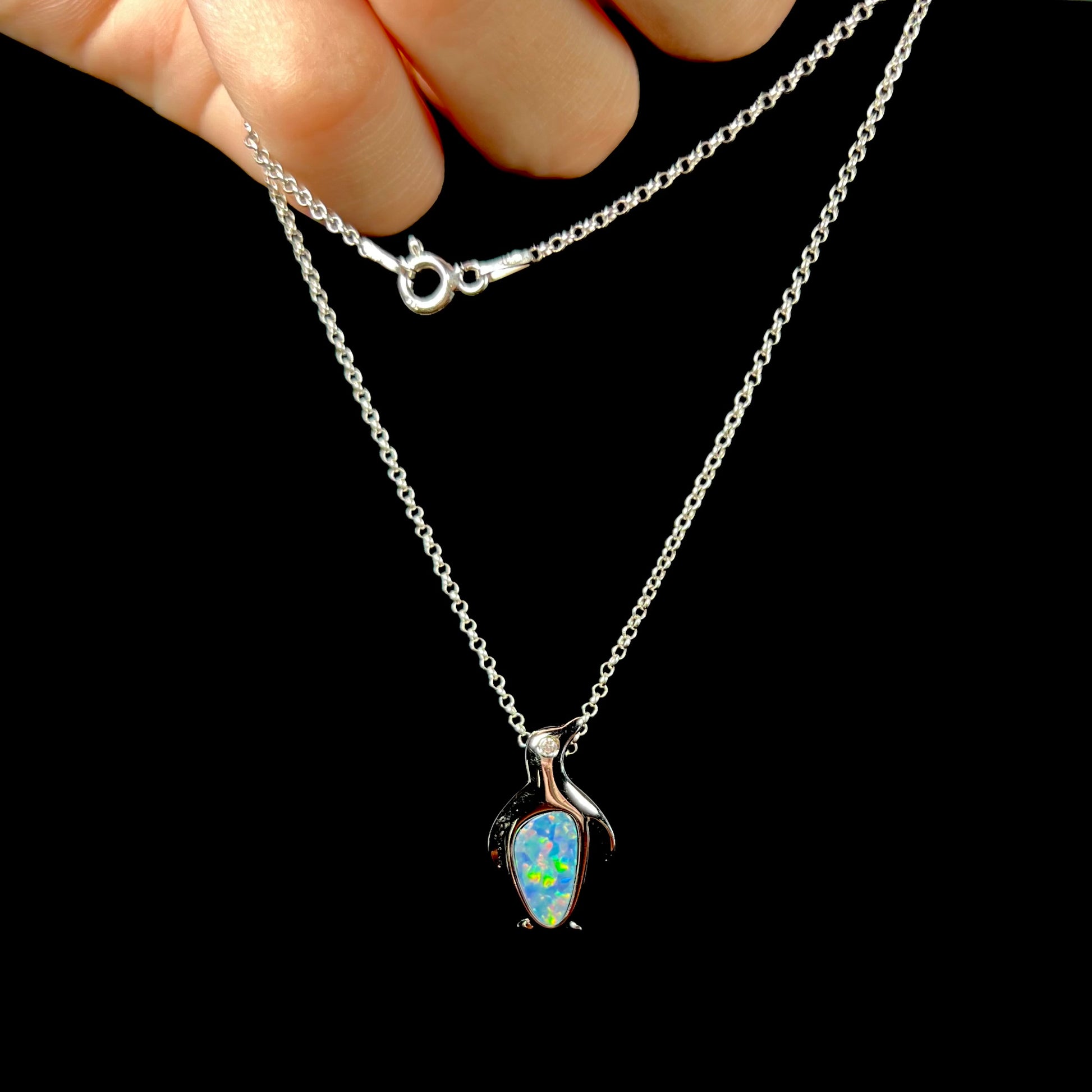 A sterling silver penguin necklace inlaid with a black opal doublet and a CZ accent in the penguin's eye.