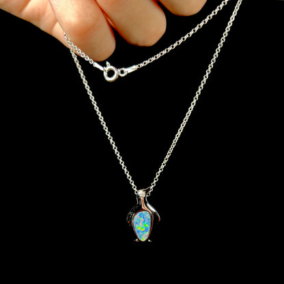 A sterling silver penguin necklace inlaid with a black opal doublet and a CZ accent in the penguin's eye.