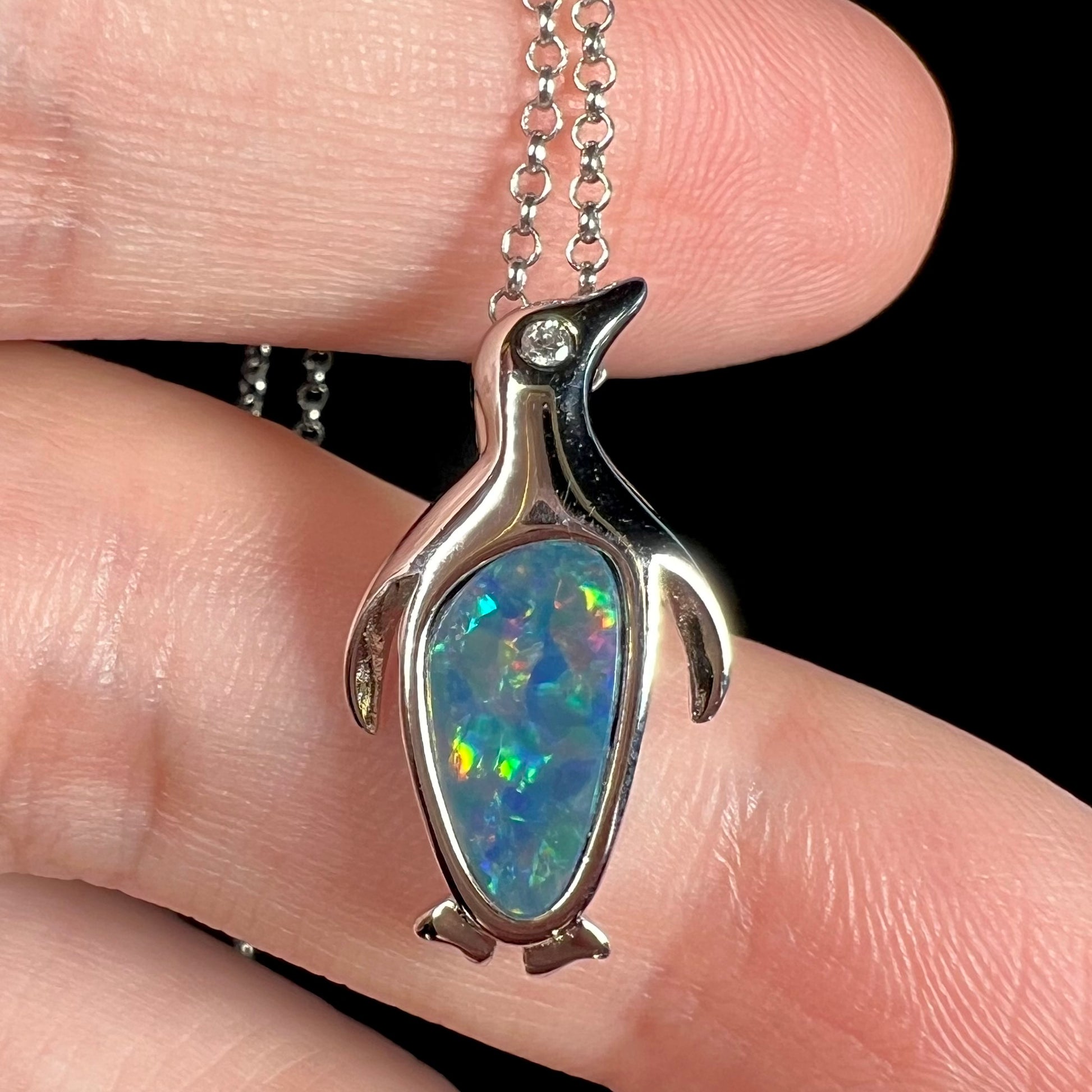 A sterling silver penguin necklace inlaid with a black opal doublet and a CZ accent in the penguin's eye.